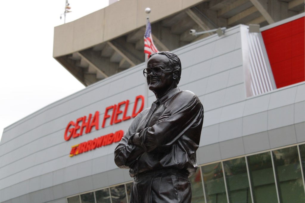 A bronze statue of Lamar Hunt with his arms folded stands in front of Kansas City Chiefs' Arrowhead Stadium.