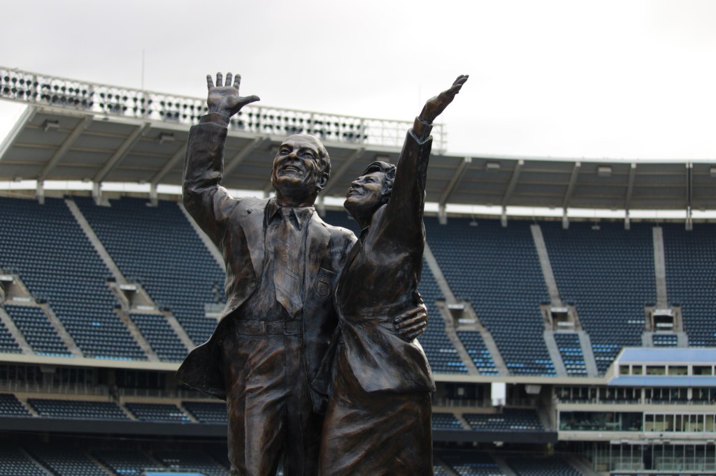 A bronze statue of Ewing Kauffman and Muriel Kauffman with joyful smiles stands in the outfield at Kansas City Royals' Kauffman Stadium.
